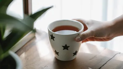 High angle of crop faceless person placing mug of hot aromatic delicious tea on wooden table