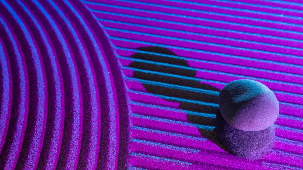 Stacked stones casting shadows on a vibrant, textured surface under blue and pink lights.