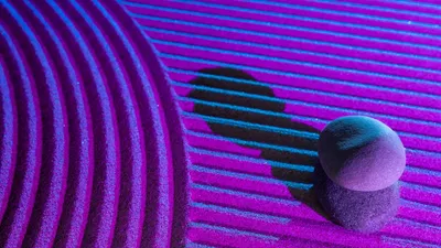Stacked stones casting shadows on a vibrant, textured surface under blue and pink lights.