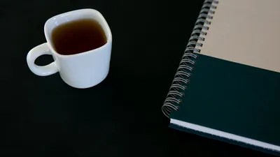 Close-up of a white tea cup and a spiral notebook on a black background. Perfect for themes of productivity and simplicity.