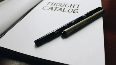 Open thought catalog notebook with pens on a wooden desk, ideal for writing inspiration.