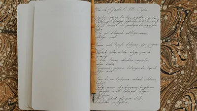 Open notebook showcasing calligraphy with a wooden pen on a brown marbled surface.