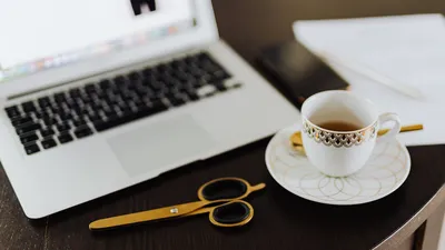 Stylish workspace featuring a laptop, tea cup, and stationery on a wooden table.