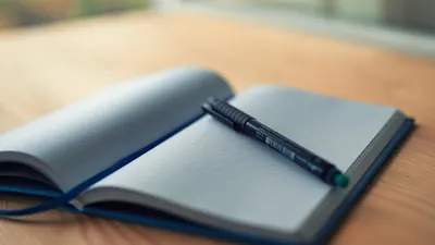 An open lined notebook with a pen resting on a wooden desk, capturing a moment of creativity.