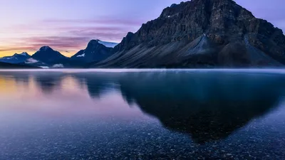 Serene sunrise over calm lake reflecting rugged mountains in Banff National Park.