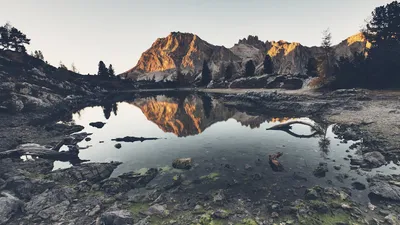 Serene mountain landscape with a lake reflecting the sunset hues, creating a tranquil scene.